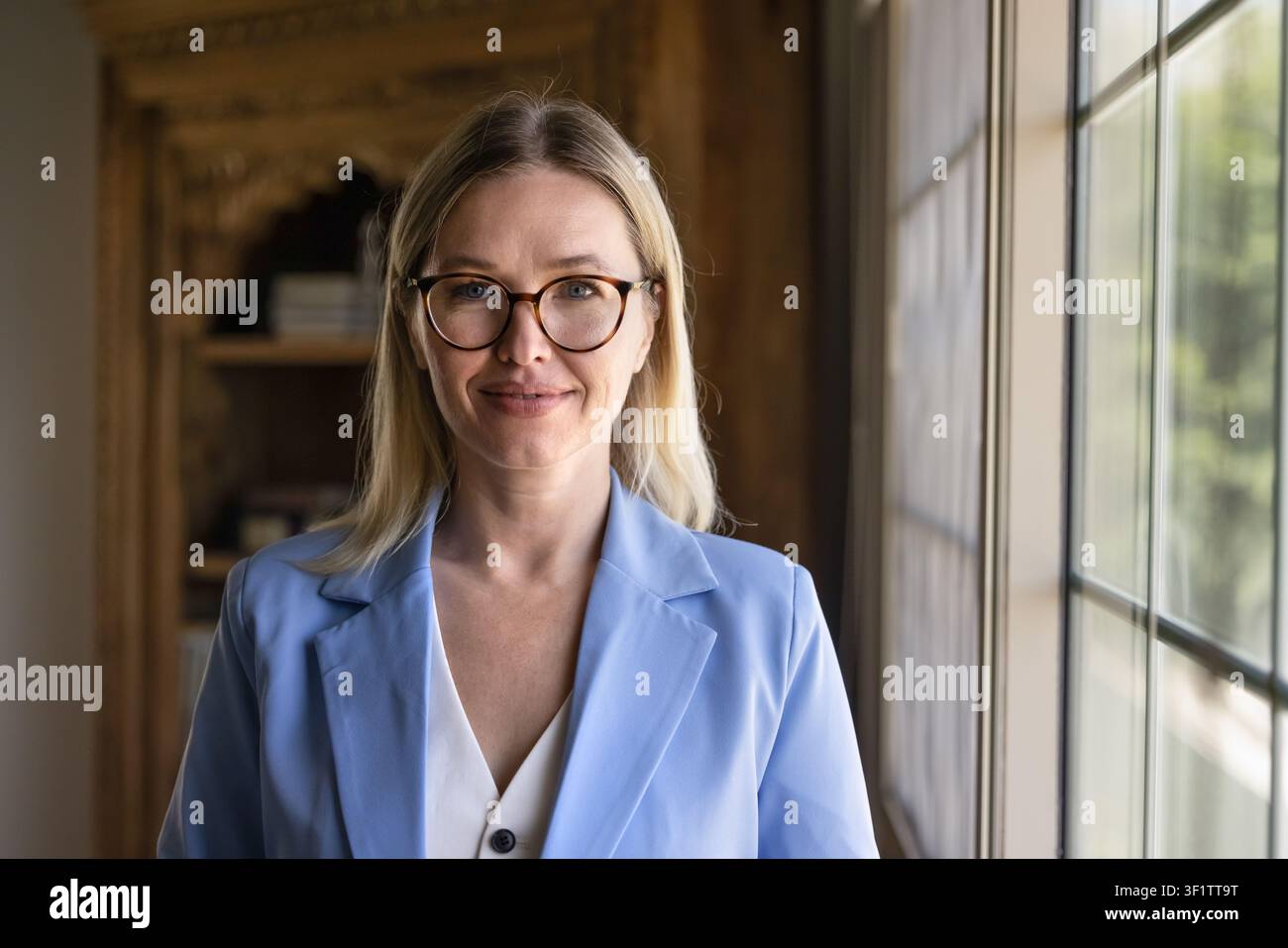 Donna caucasica che sorride alla telecamera posando in un ufficio domestico Foto Stock