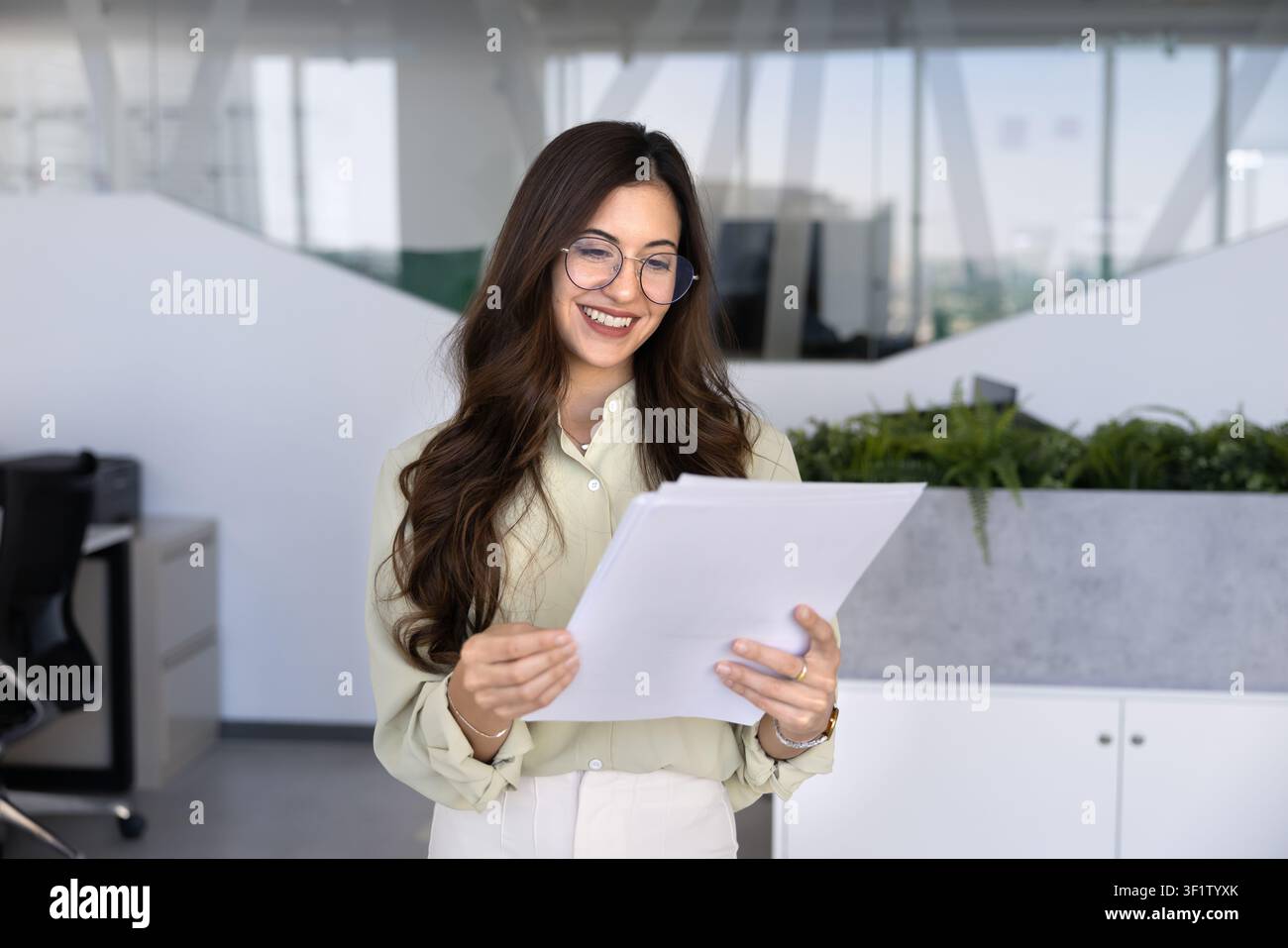 Donna professionista sorridente in piedi in un ufficio aziendale mentre legge documenti Foto Stock