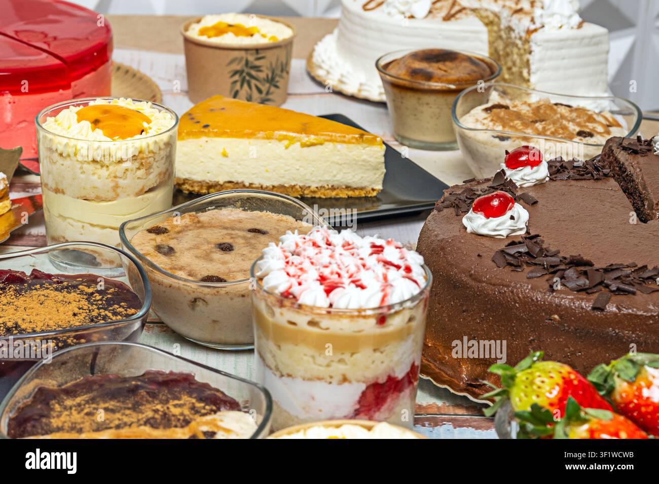 Prima piano di dessert assortiti con una ricca torta al cioccolato con ciliegie, una fetta di cheesecake, parfaits a strati e vari budini cremosi in vetro Foto Stock