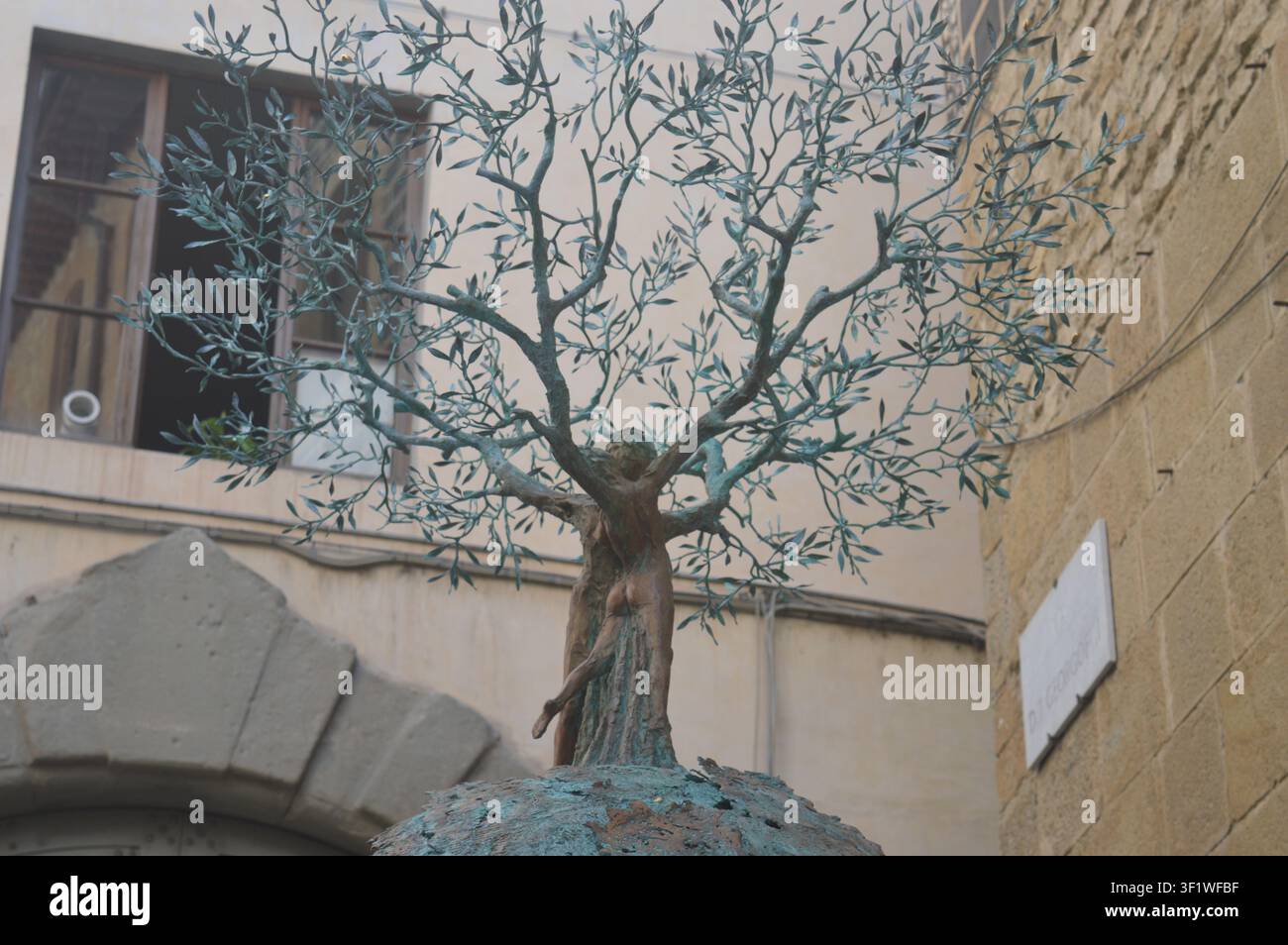 Scultura in bronzo di un albero che incorpora figure umane davanti agli edifici storici in pietra di Firenze, Italia. Foto Stock