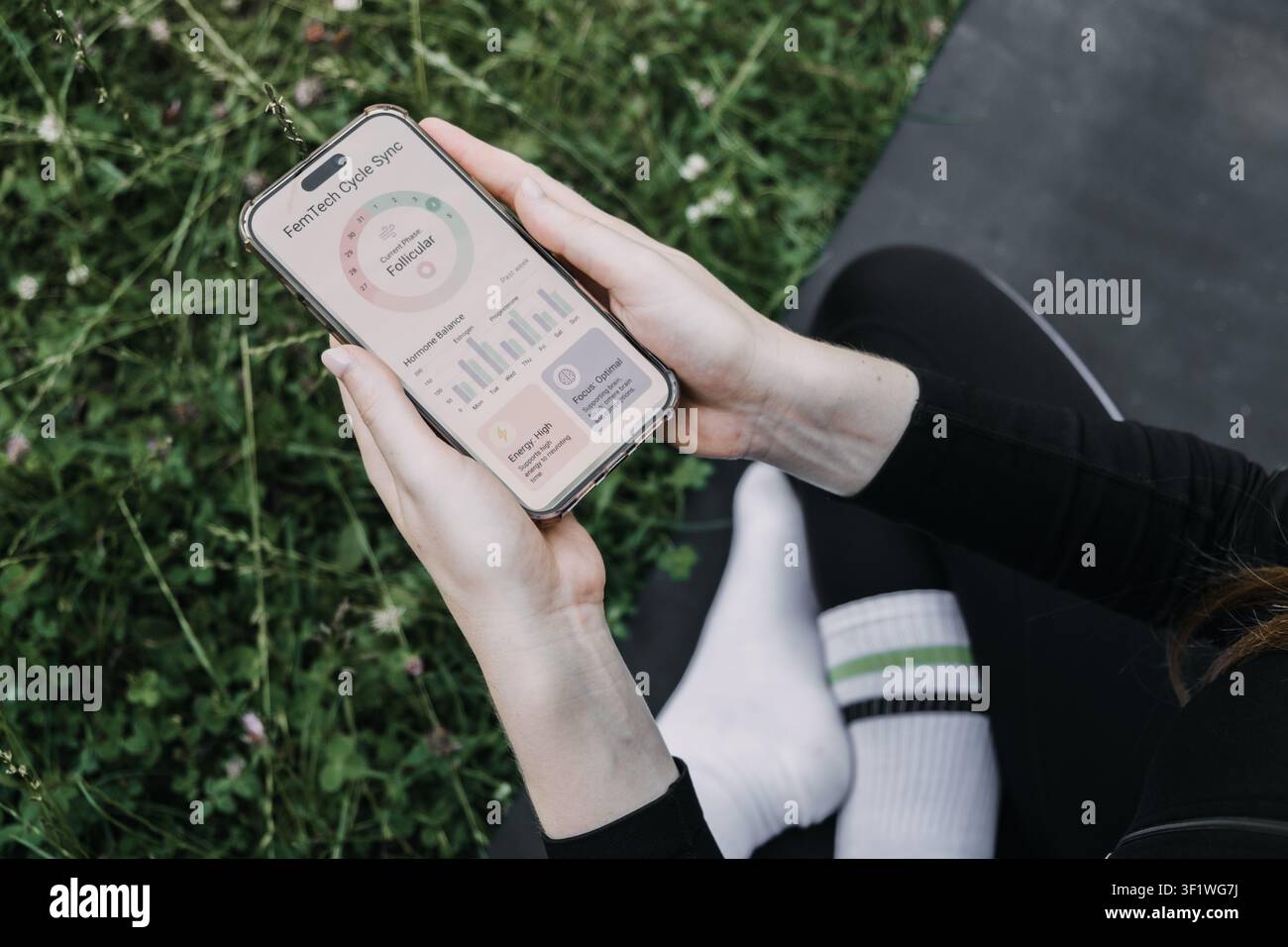 Mani che tengono uno smartphone che mostra l'interfaccia di un'applicazione di sincronizzazione del ciclo FemTech all'aperto. Monitoraggio dell'equilibrio ormonale, consapevolezza delle fasi del ciclo, ormonale Foto Stock