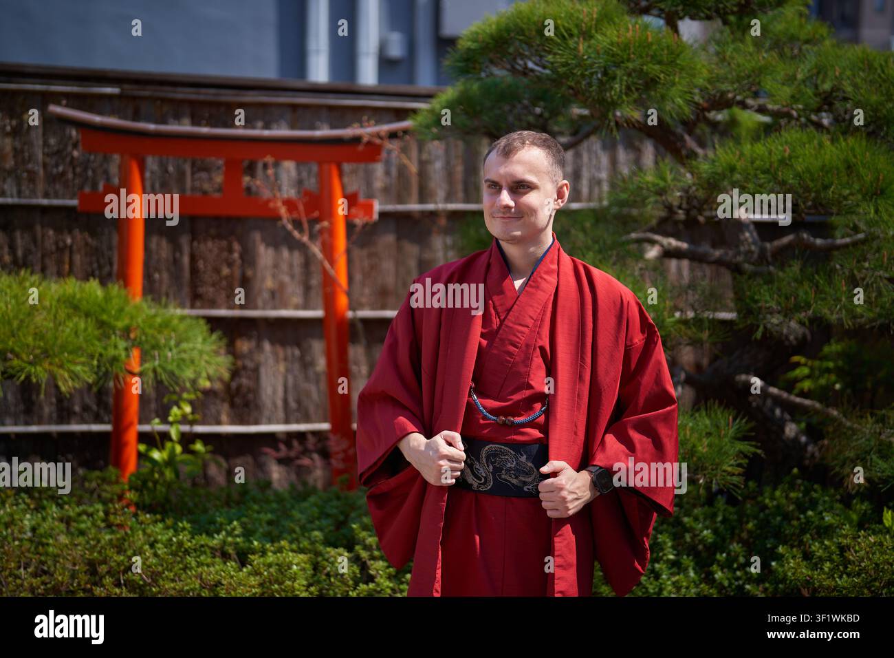 Uomo in kimono rosso di fronte a un cancello torii Foto Stock