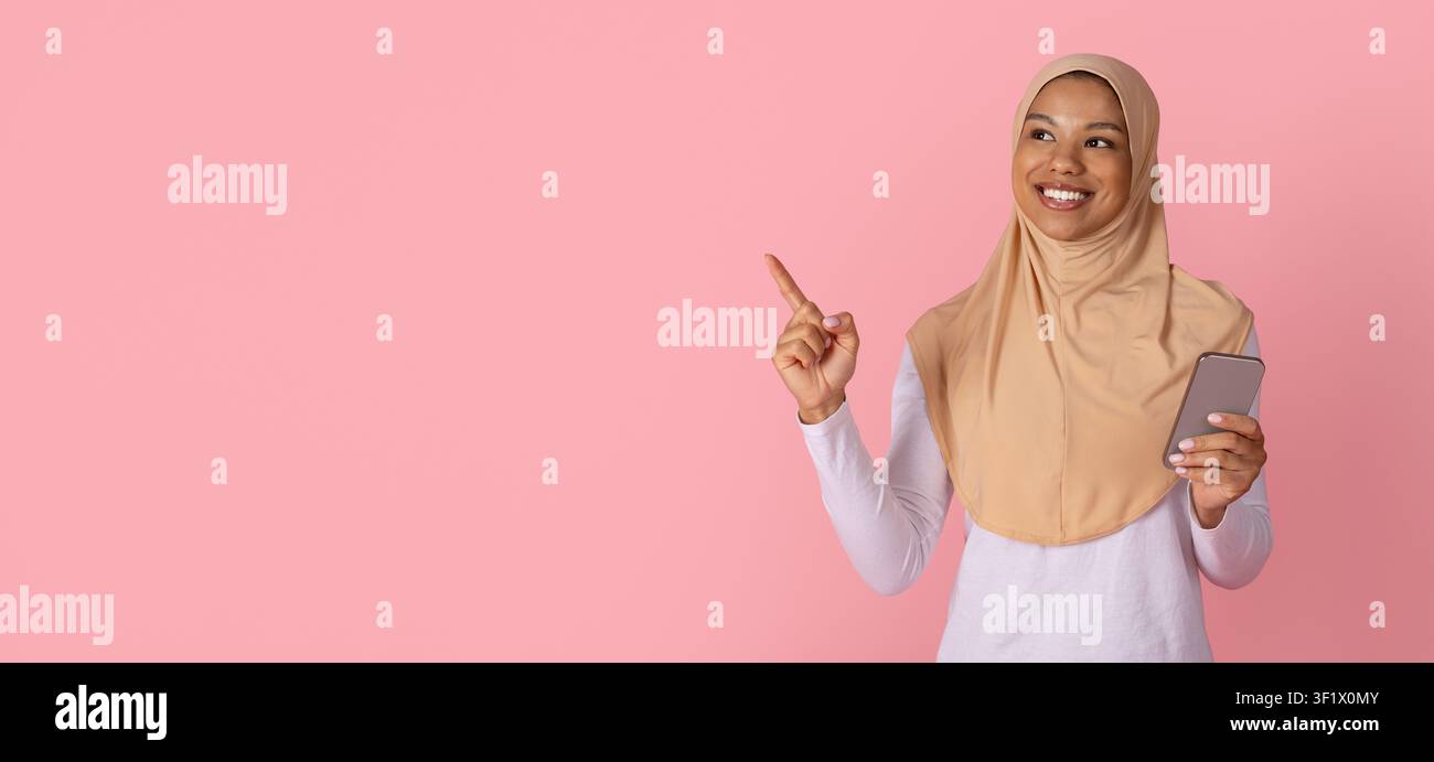 Donna musulmana nera in hijab che tiene uno smartphone e indica uno spazio di copia Foto Stock