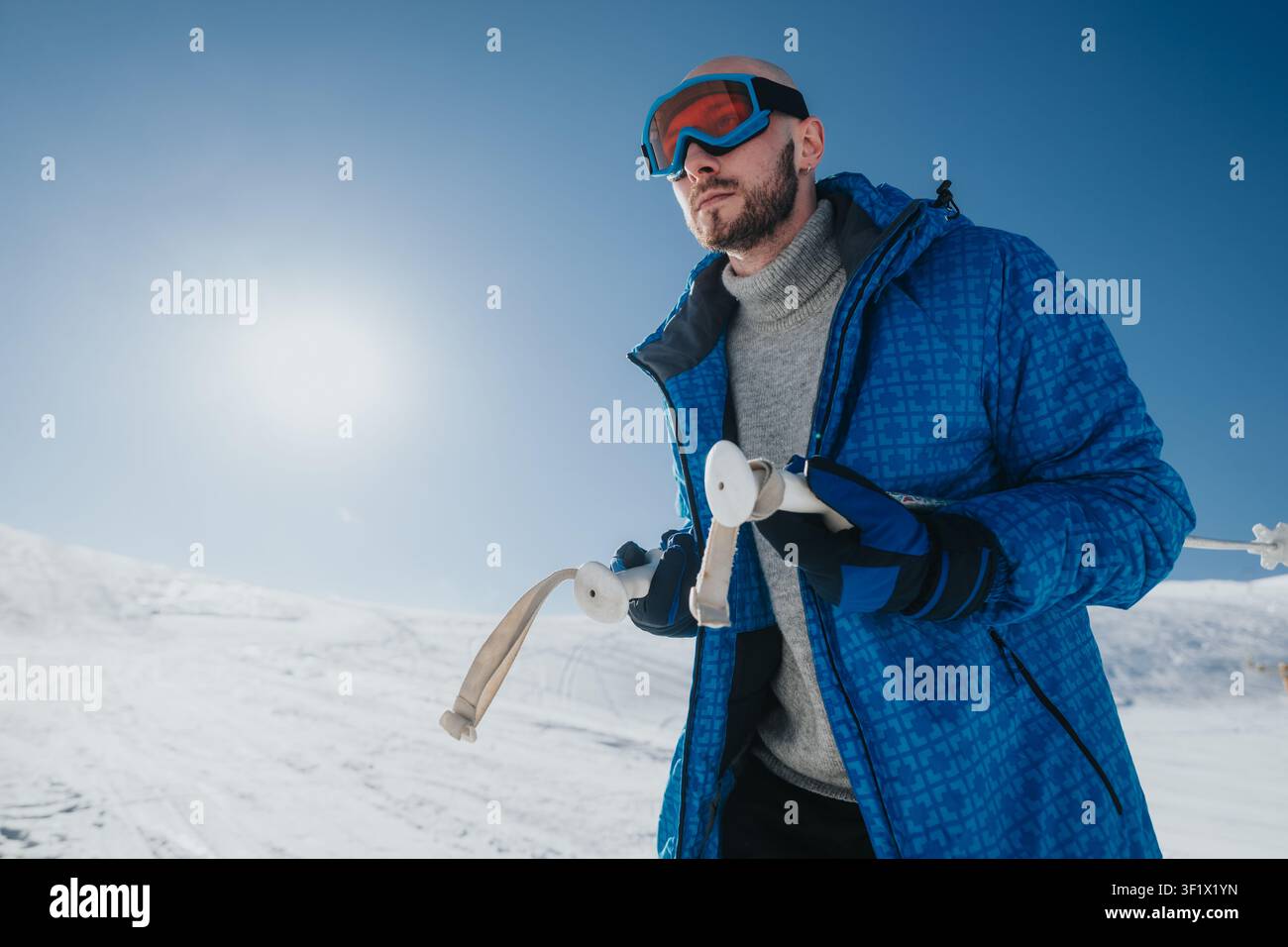 Uomo in giacca blu che tiene la corda del teleferico su una pendice innevata e soleggiata con occhiali da sci Foto Stock