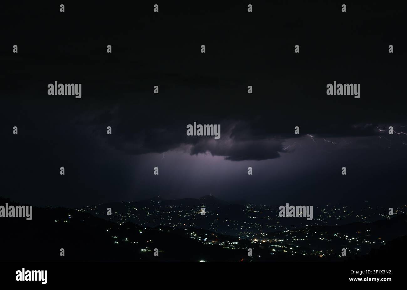 Una scena notturna drammatica sull'Himalaya che mostra un fulmine che colpisce sopra una città di montagna nell'Himachal Pradesh con le luci della città che brillano. Foto Stock