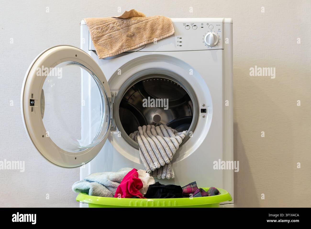 Lavatrice aperta con la biancheria che sporge e un cesto di vestiti colorati sotto. Elettrodomestico, biancheria pulita e nessuna persona. Foto Stock