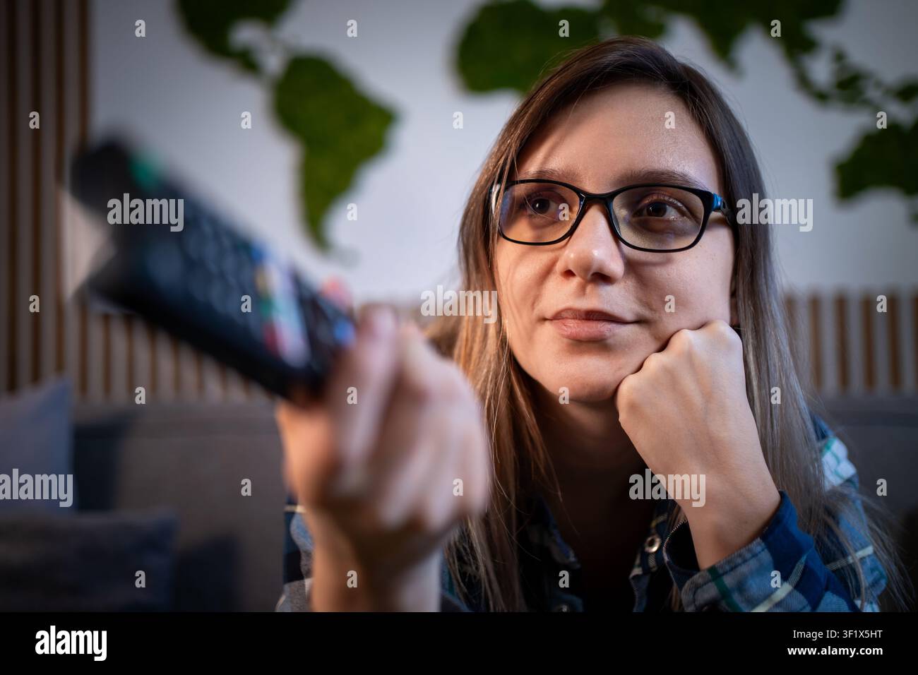 Stanca di guardare la televisione. Giovane donna annoiata con gli occhiali seduta sul divano e che cambia i canali TV con il telecomando. Foto Stock