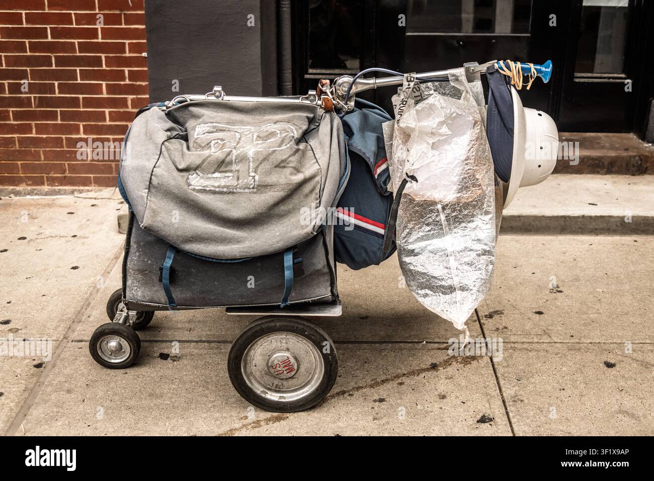 Il carrello di un portalettere USPS, carico di borse postali in tela e un casco, è parcheggiato su un marciapiede di New York City. Foto Stock