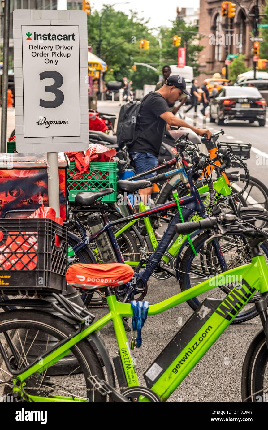 I corrieri in bicicletta aspettano fuori dal molo di carico di un negozio di alimentari per ritirare gli ordini Instacart a New York Foto Stock