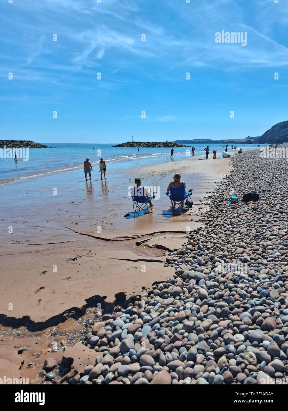 Le persone si rilassano durante l'ondata di caldo sulla spiaggia in parte ghiaiosa e in parte sabbiosa a Sidmouth, Devon Foto Stock