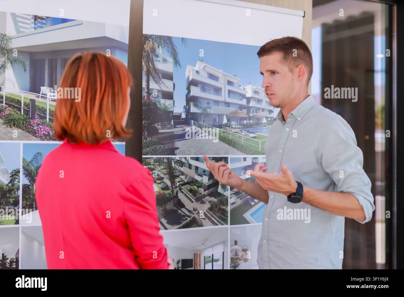 Agente immobiliare che spiega i progetti architettonici di un nuovo complesso residenziale a un cliente, discutendo le opzioni di investimento immobiliare e sviluppo Foto Stock