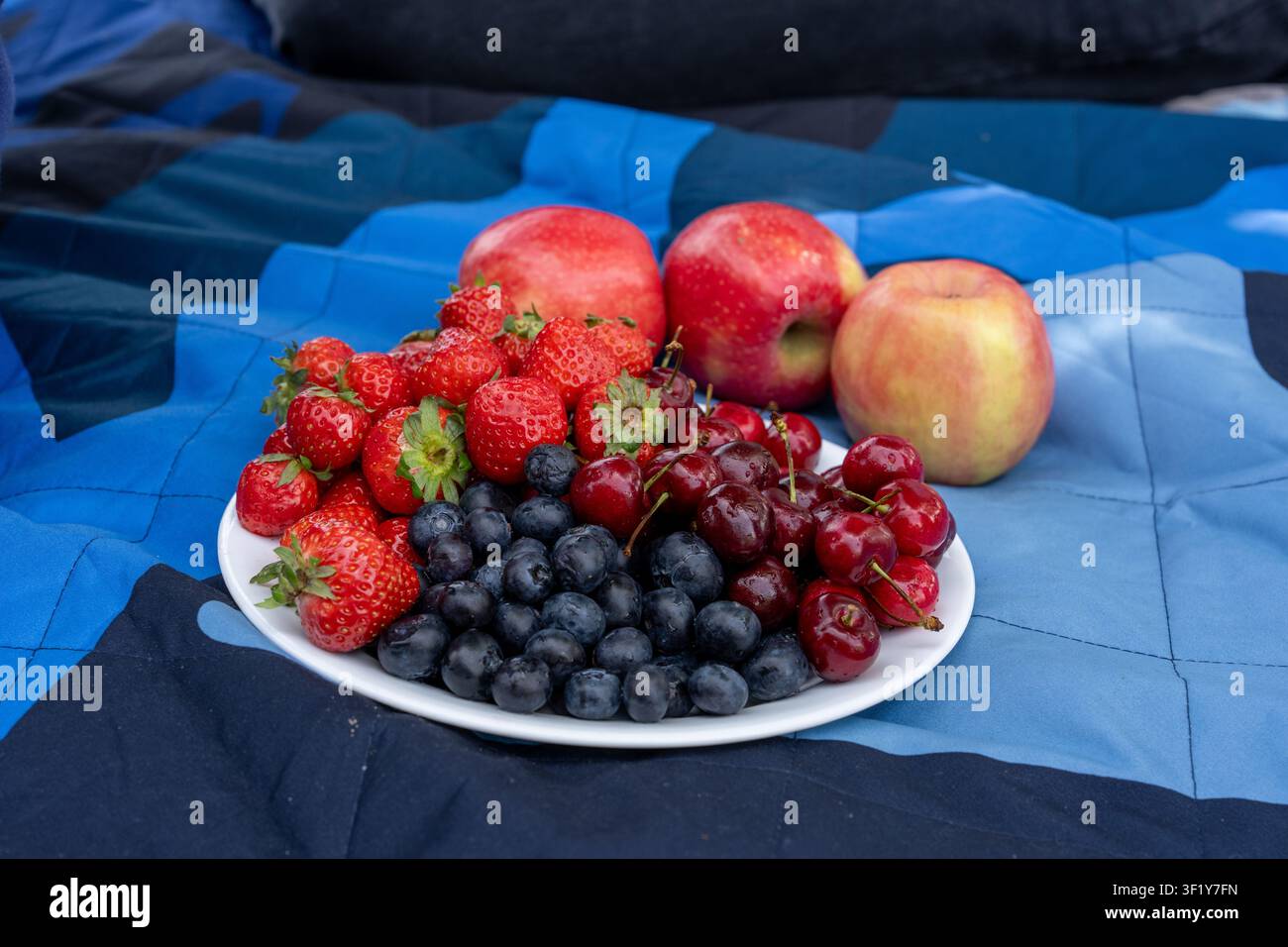 Un primo piano orizzontale ad alta angolazione di un piatto bianco pieno fino all'orlo di fragole fresche mature, mirtilli e ciliegie dolci, posizionato accanto t Foto Stock