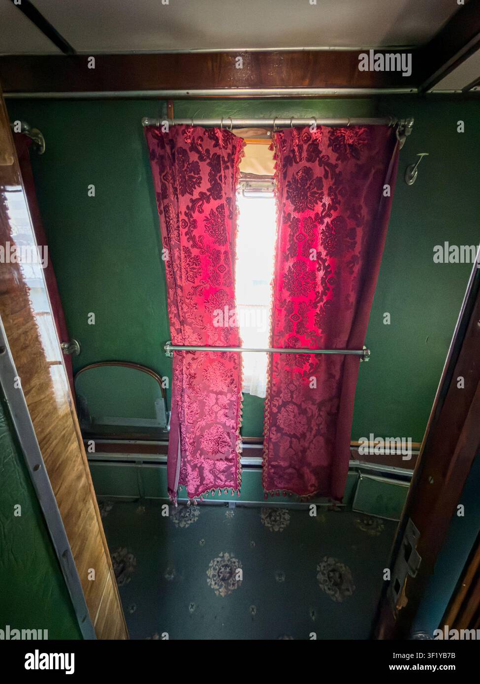 Interno vintage di un treno passeggeri con lussuosi tende floreali rosse, eleganti pannelli in legno, pareti verde scuro, luce naturale dalle finestre, naso accogliente Foto Stock