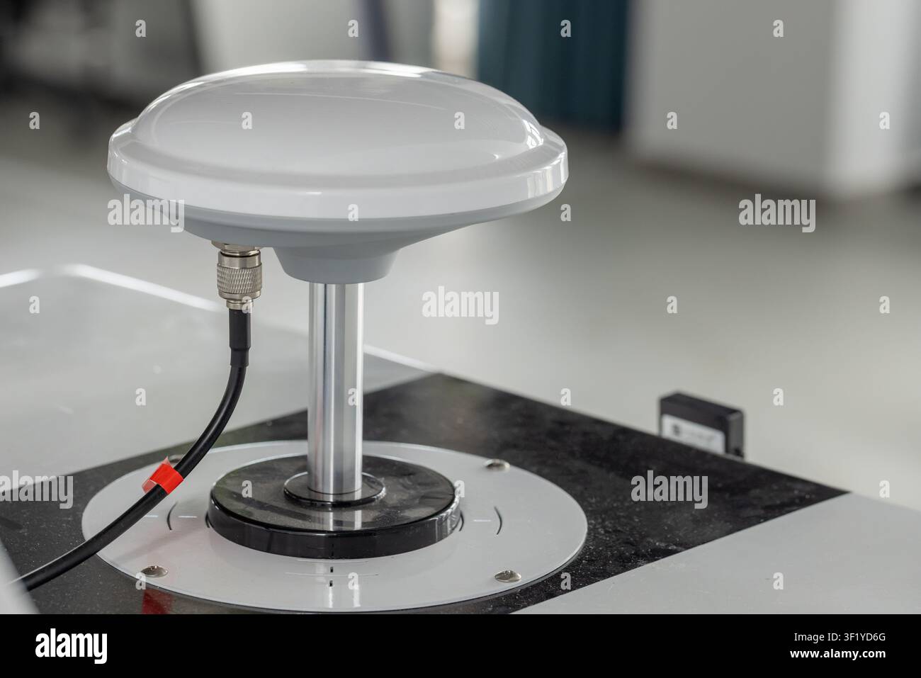 Antenna GPS a cupola bianca montata su un piedistallo metallico con collegamento a cavo coassiale, fotografata in un ambiente di laboratorio pulito. Adatta per la tecnologia Foto Stock