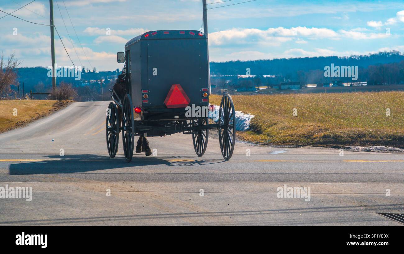 Un calesse trainato da cavalli procede lungo una strada di campagna fiancheggiata da erba e campi. Il cielo è sereno con qualche nuvola. La scena mostra la vita rurale in una zona tranquilla. Foto Stock