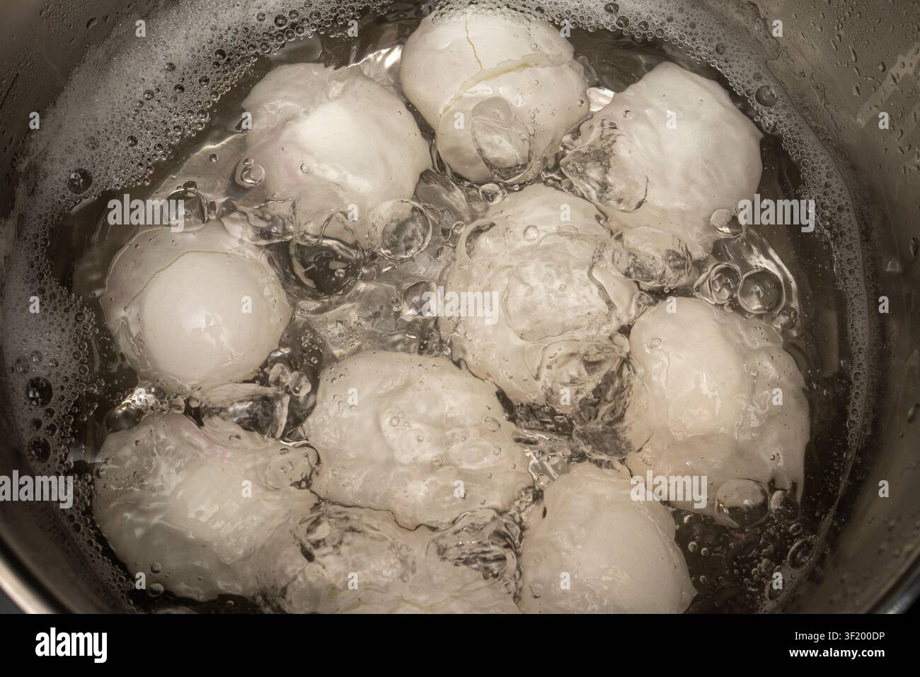 Diverse uova vengono messe in una pentola piena di acqua bollente. Le bolle salgono mentre l'acqua si riscalda. Questa attività avviene in una cucina durante la tarda mattinata Foto Stock