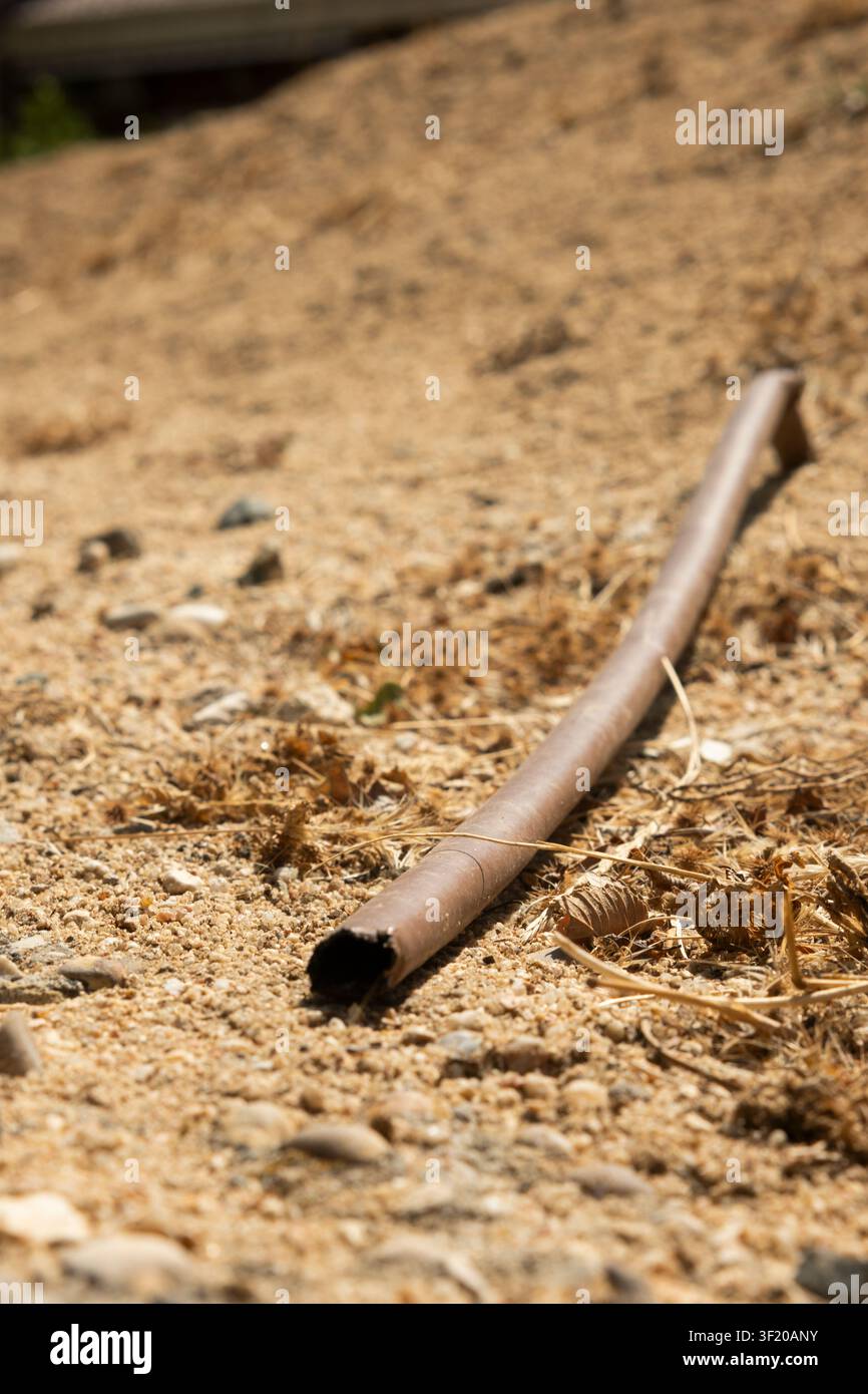 Tubo metallico arrugginito sdraiato su terreno asciutto sotto la luce del sole, che mostra abbandono Foto Stock