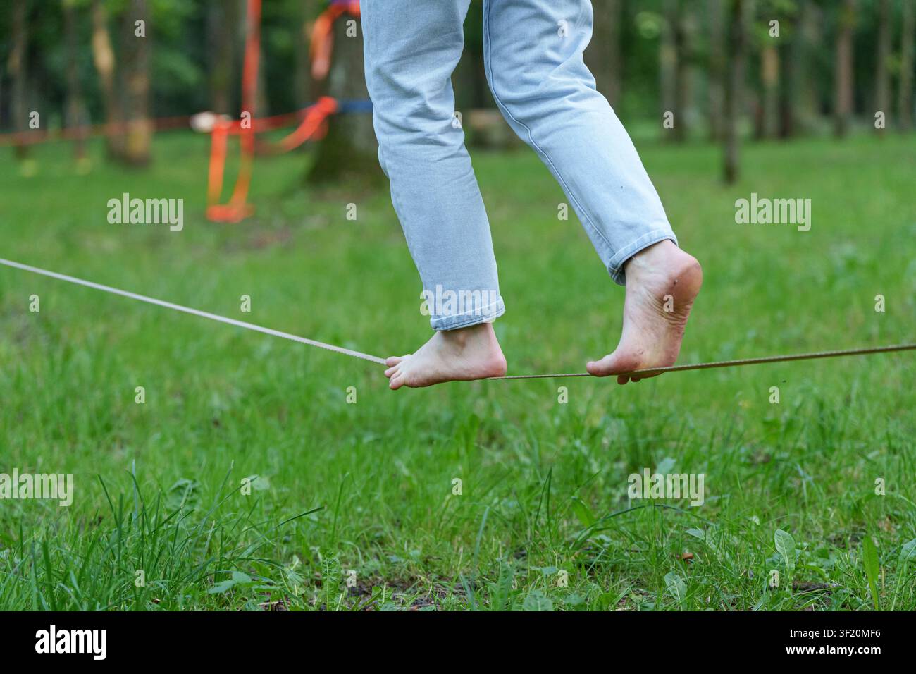 Persona scalza in equilibrio su una slackline tesa sull'erba verde nel parco, concetto di sport di slacklining all'aperto e allenamento di equilibrio. Foto Stock