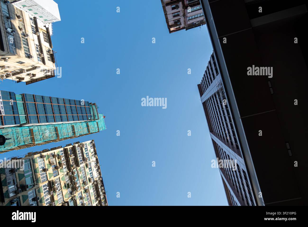 Vista ad angolo basso di un edificio denso e alto a Kowloon, Hong Kong, in costruzione avvolto in un ponteggio verde Foto Stock