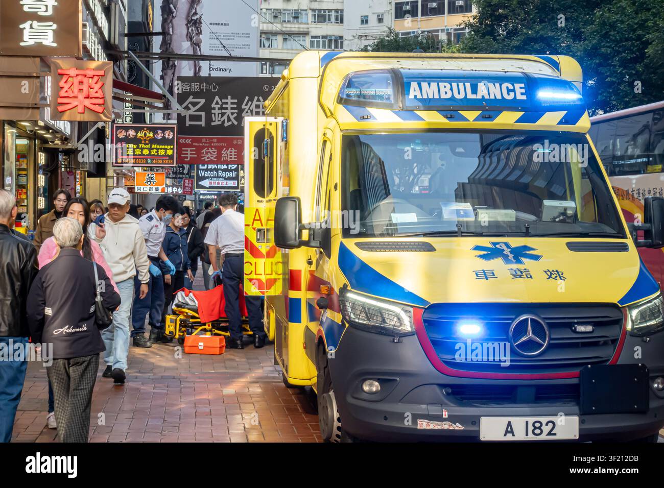 Soccorritori e primi soccorritori assistono una persona sul marciapiede. Risposta medica di emergenza in ambulanza, strada commerciale a Central, Hong Kong Foto Stock