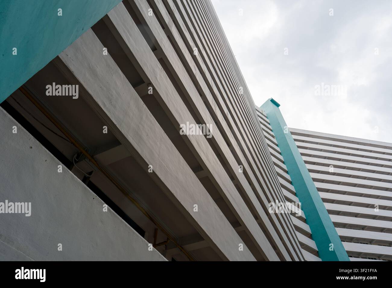 Struttura moderna in cemento con accenti turchesi. Linee geometriche audaci definiscono il design architettonico. Il cielo forma uno sfondo morbido dietro l'edificio. Vertica Foto Stock