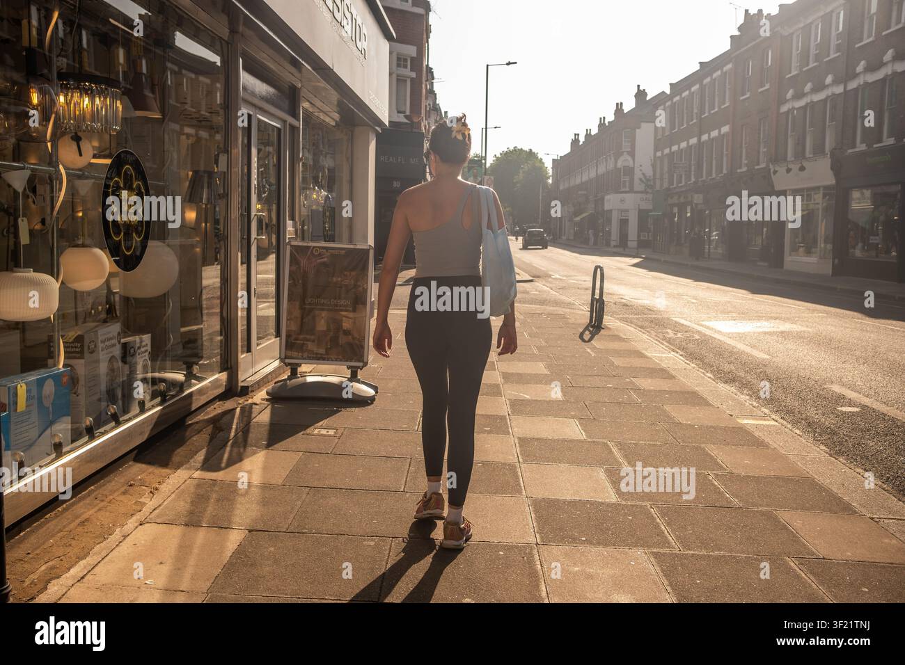LONDRA - 27 MAGGIO 2026: Nuova Kings Road, Fulham – Donna che passa davanti ai negozi nella calda luce della sera vicino a Parsons Green. Foto Stock