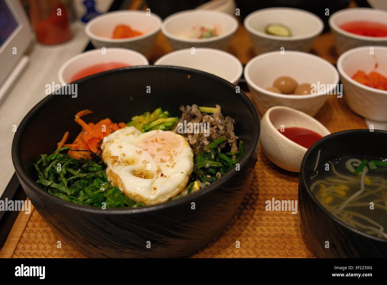 Bibimbap coreano con riso, verdure e uovo fritto servito in una ciotola nera con contorni, Corea del Sud Foto Stock