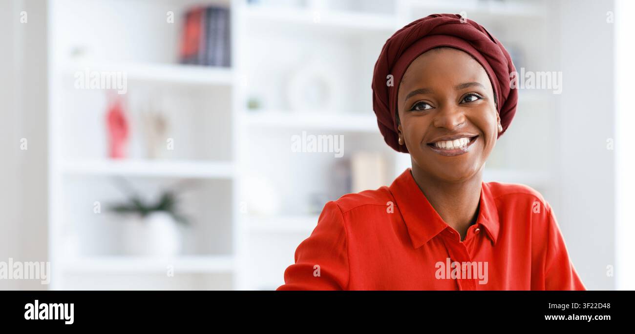 Donna con foulard sorride in una stanza luminosa piena di libri e piante Foto Stock