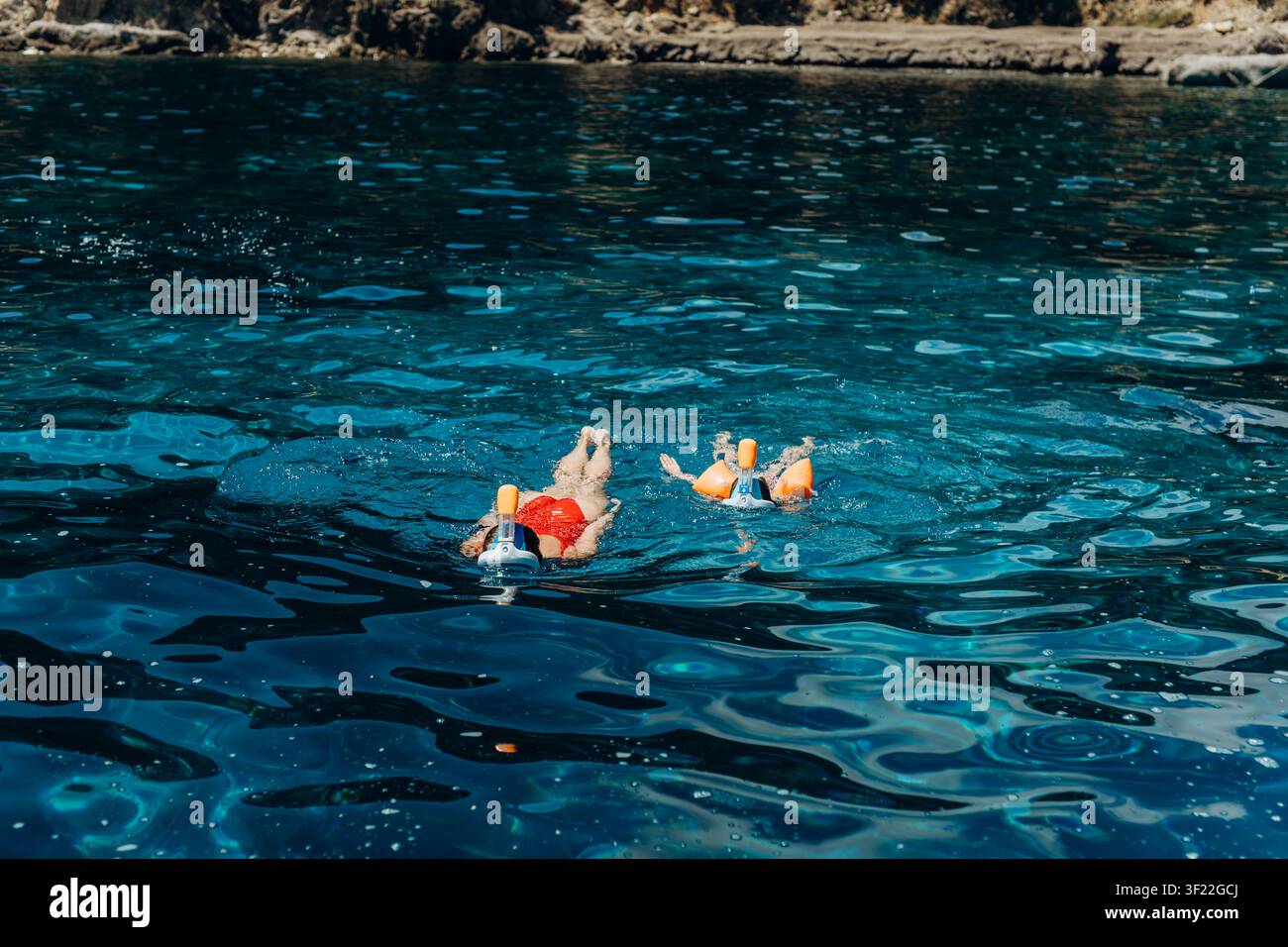Snorkelisti galleggiano insieme nel mare sotto una costa rocciosa in una luminosa giornata estiva. Escursioni di snorkeling costiere e turismo marino che ispirano le famiglie Foto Stock