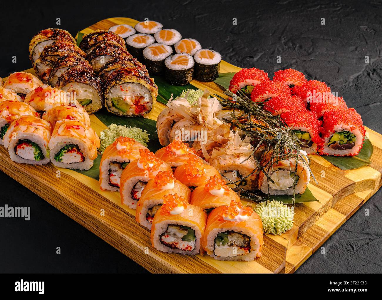 Diversi tipi di sushi sono disposti su una tavola di legno. Il sushi include rollini con varie farciture e condimenti. Il wasabi verde è servito come contorno. Foto Stock