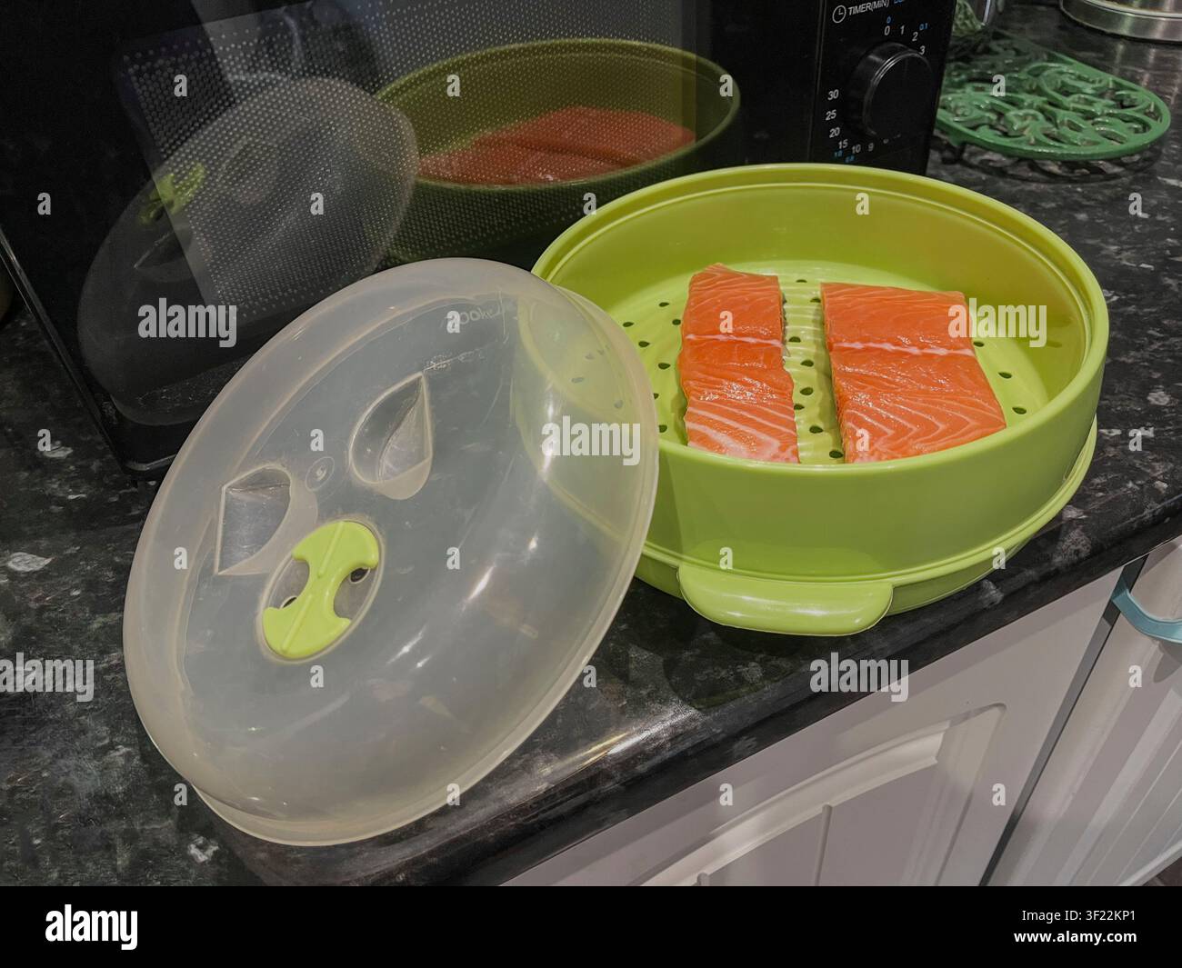 Filetti di salmone in un vaporetto per microonde in plastica pronti per essere cotti. Sul piano di lavoro della cucina accanto al microonde. Foto Stock