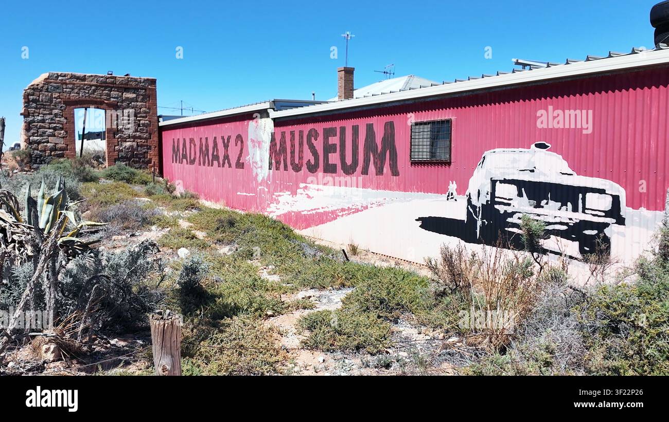 Silverton, Nuovo Galles del Sud, Australia – 12 dicembre 2024: Vista del Museo Mad Max 2, con un muro di lamiera ondulata rossa con grafiche cinematografiche e una pietra Foto Stock