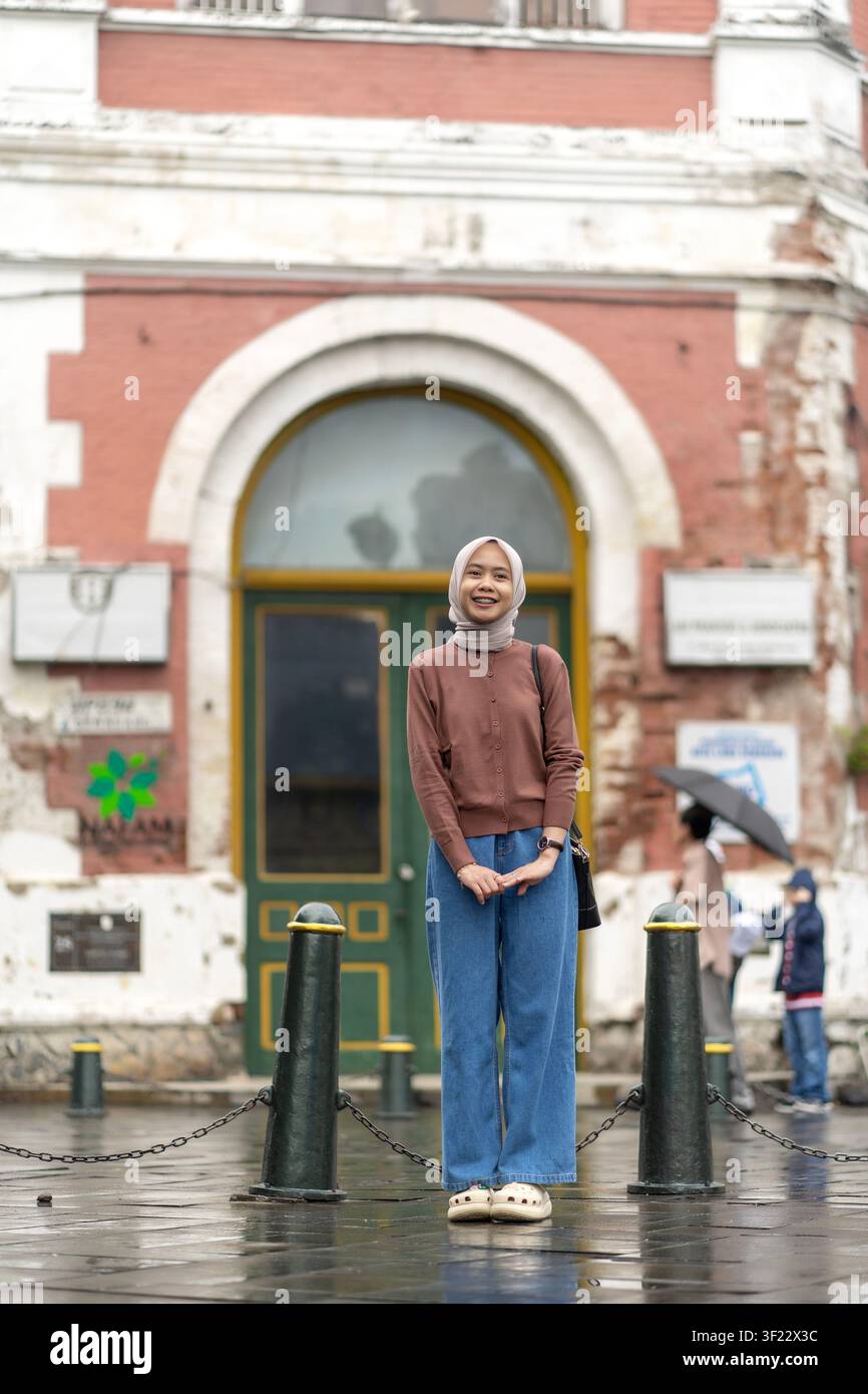Donna musulmana indonesiana asiatica con hijab sorridente, in piedi davanti a un vecchio edificio a Kota Lama Semarang. Viaggiatrice gioiosa che esplora l'er dell'Indonesia Foto Stock