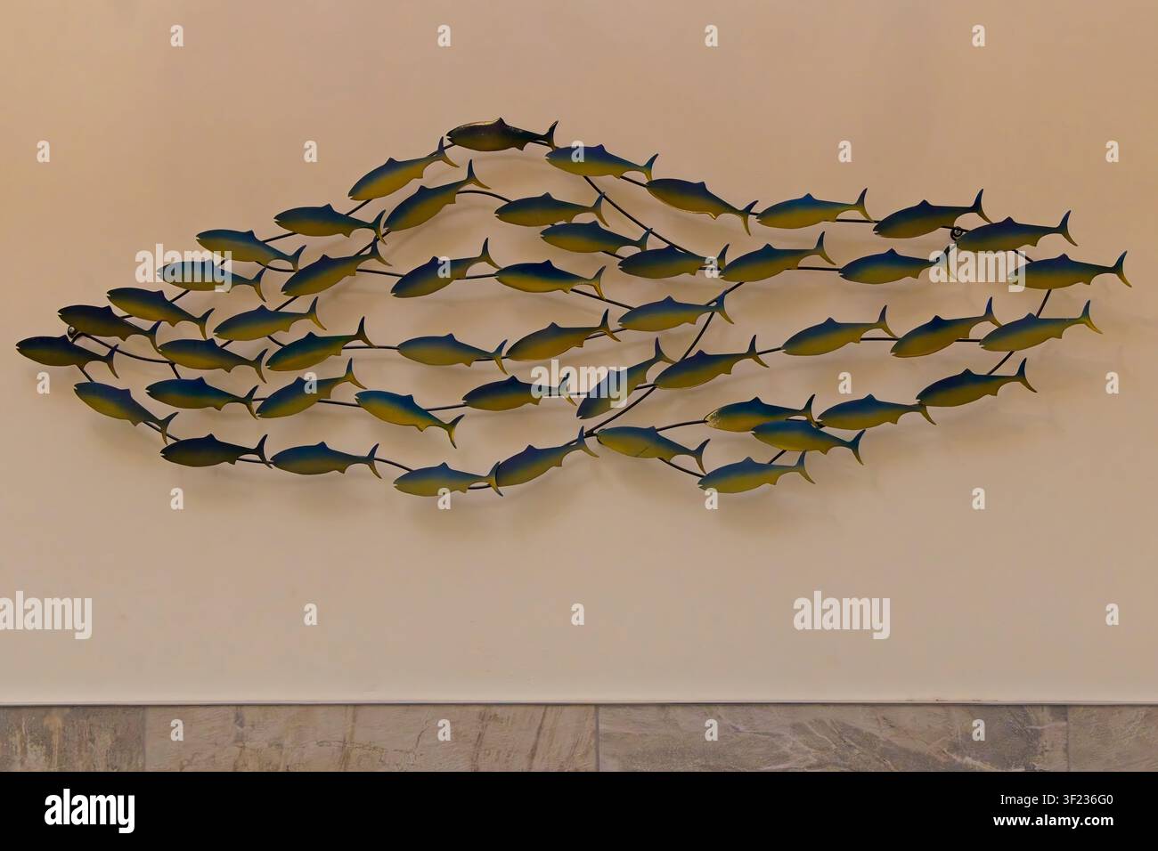 Una grande scultura murale in metallo che raffigura una scuola di pesci blu e gialli che nuotano, montata su una parete interna neutra. Foto Stock