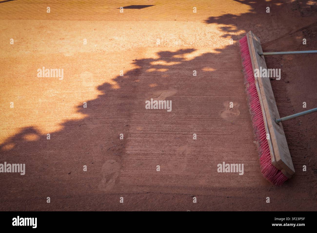 Grande scopa a spinta che spazza il terreno esterno polveroso con ombre di alberi in condizioni meteorologiche soleggiate Foto Stock
