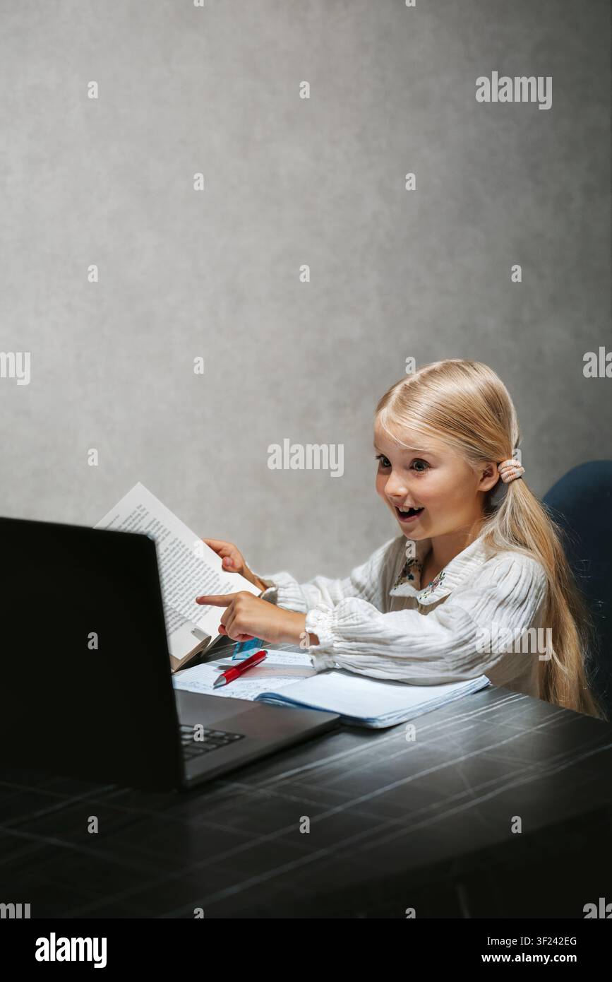 Bambino delle scuole elementari che studia online su laptop, ragazza curiosa che legge e scrive durante un'interessante lezione online di homeschooling digitale Foto Stock