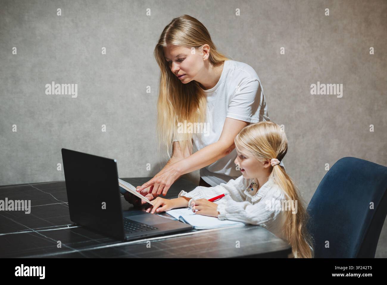 Madre che aiuta sua figlia a studiare la lezione nella scuola online con laptop a casa, bambino che utilizza l'istruzione digitale a casa stile di vita familiare apprendimento t Foto Stock