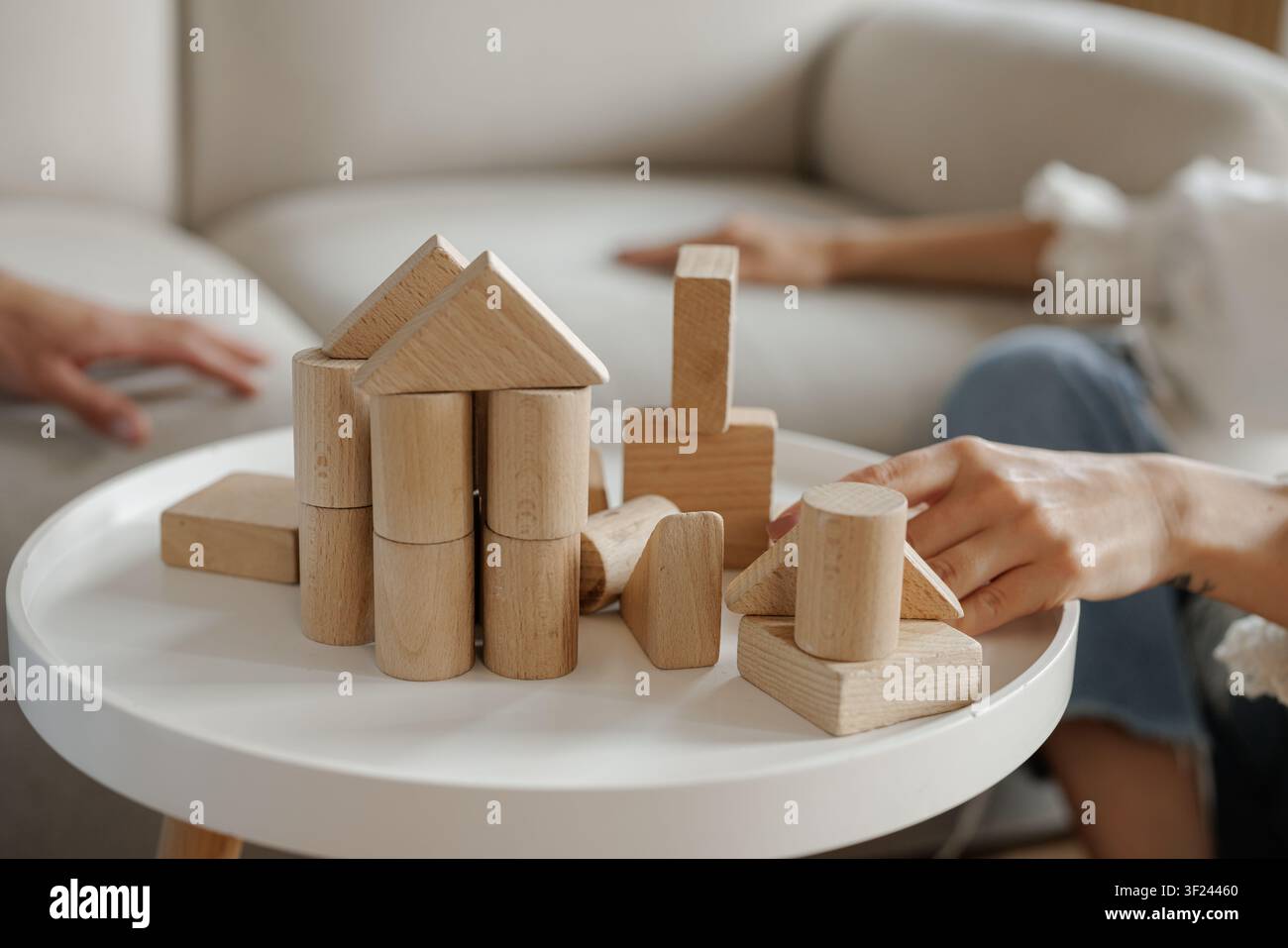 Una famiglia si impegna in un gioco creativo, costruendo una casa ecologica con blocchi di costruzione in legno su un tavolo bianco, promuovendo il legame familiare e la sostenibilità Foto Stock