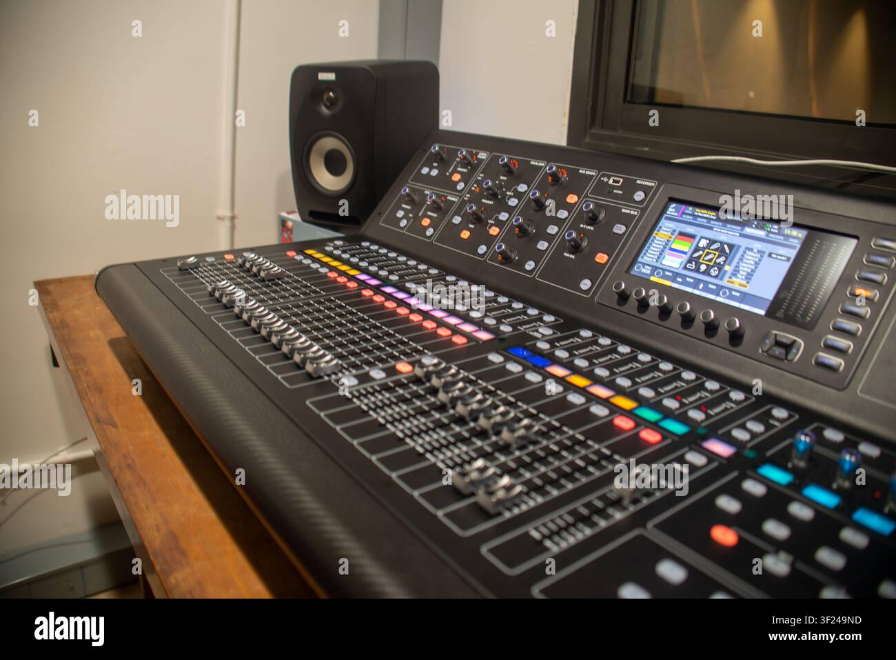 Questa immagine mostra una console di mixaggio audio digitale professionale su una scrivania di legno in uno studio di registrazione, dotata di vari controlli, display e connessioni Foto Stock