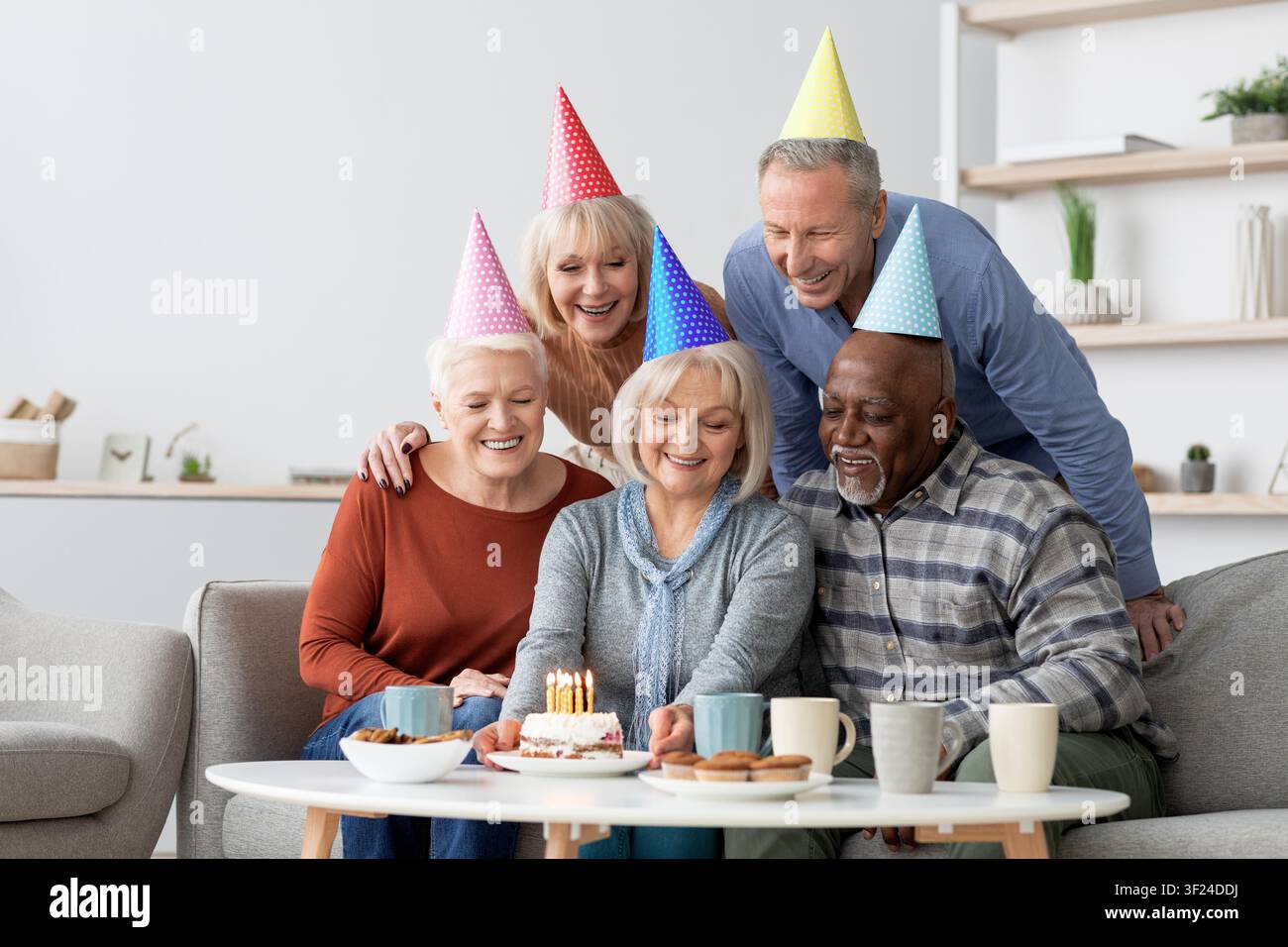 Gruppo diversificato e felice di anziani che celebrano il compleanno con torta e candele a casa, concetto familiare Foto Stock