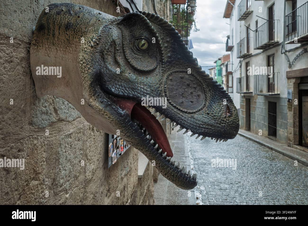 Scultura a testa di dinosauro che emerge da un vecchio muro di pietra nel villaggio medievale di Morella, Castellón, Spagna. Foto Stock