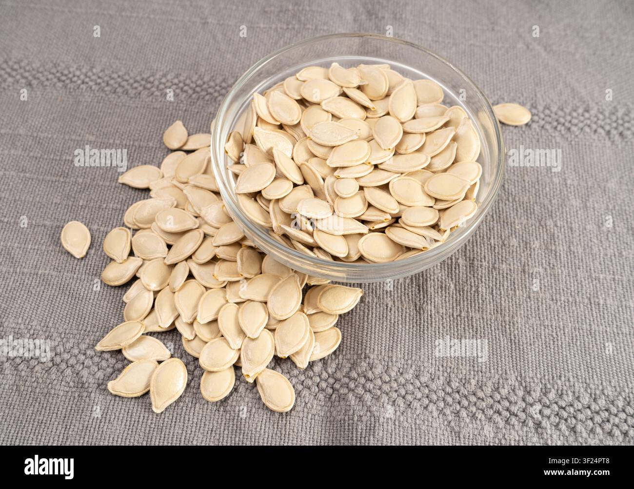 Semi di zucca interi con guscio, grani di pepita crudi, noci verdi sane sparse, seme di zucca con buccia su tovagliolo grigio vista dall’alto Foto Stock