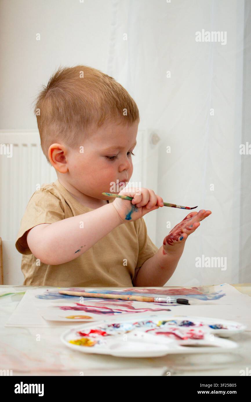 Bambino che mescola acquerelli con le dita sulla carta. Apprendimento tattile sulla miscelazione dei colori. Il gioco sensoriale rafforza le connessioni neurali. Terapia artistica e ar Foto Stock