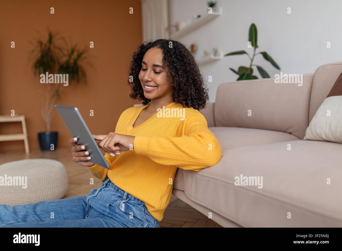 Giovane donna afroamericana sorridente che utilizza un tablet seduta sul divano a casa Foto Stock
