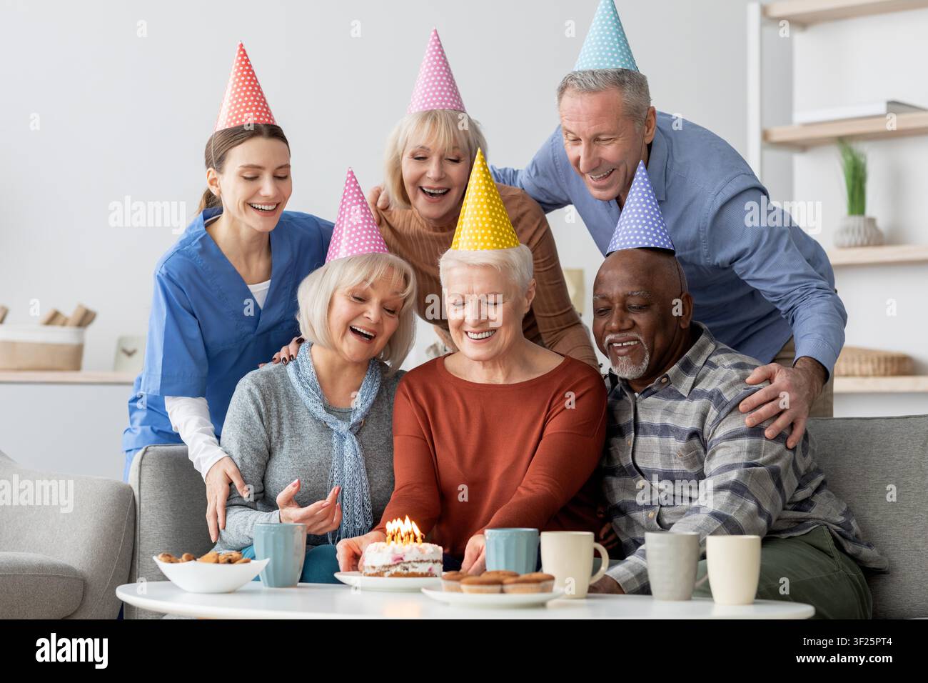 Gruppo felice di anziani che celebrano insieme un compleanno in un accogliente soggiorno, momento gioioso Foto Stock