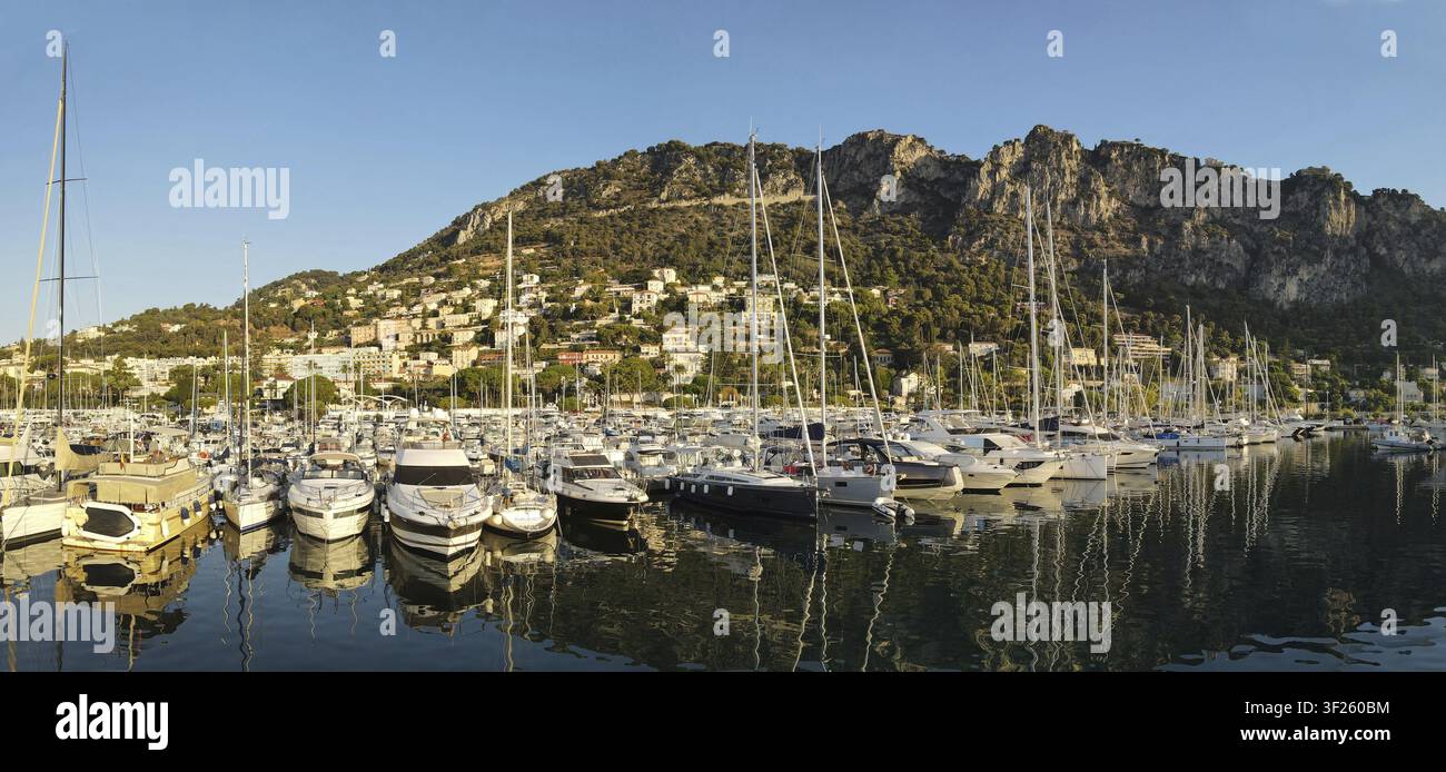 Una marina con numerose barche e yacht contro uno sfondo montuoso al tramonto, che si riflettono in acque calme, Fotografia a droni, Beaulieu-sur-Mer, Francia Foto Stock