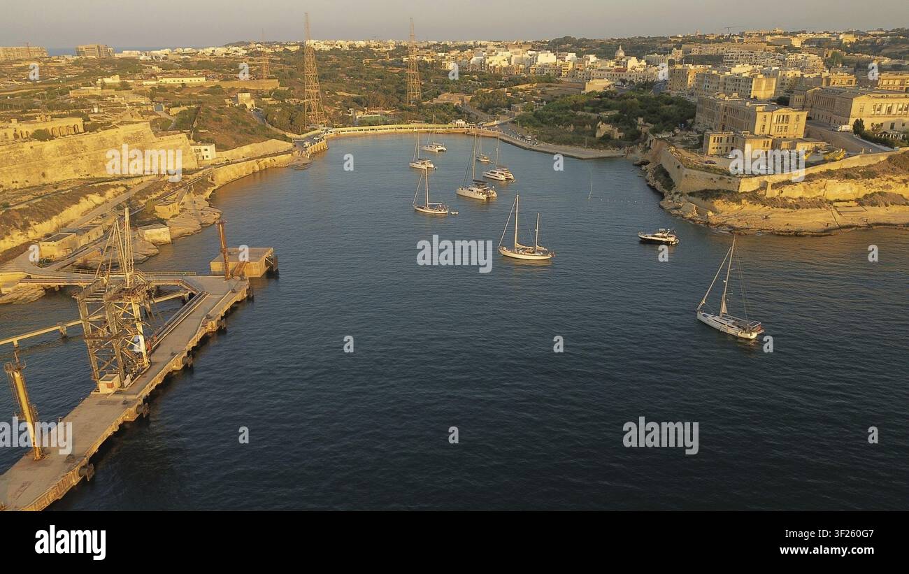 Alcune barche a vela ancorate in un porto sereno illuminato dal tramonto dorato. Baia di Rinella, Malta Foto Stock