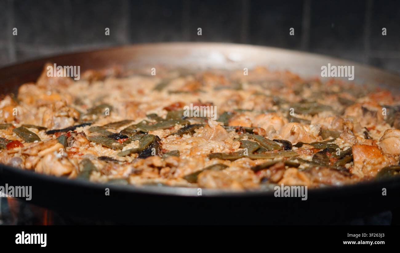 Paella spagnola che cuoce a fuoco lento in una grande padella con pollo, riso e fagiolini Foto Stock