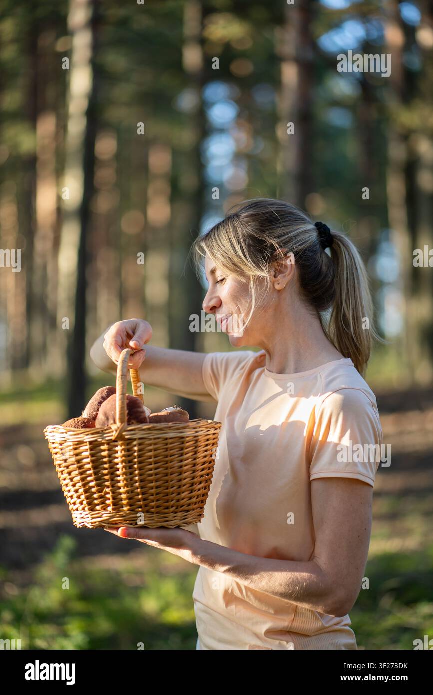 Cibi naturali e raccolta sostenibile, donna raccoglitrice positiva ha raccolto un cesto pieno di porcini. Foto Stock