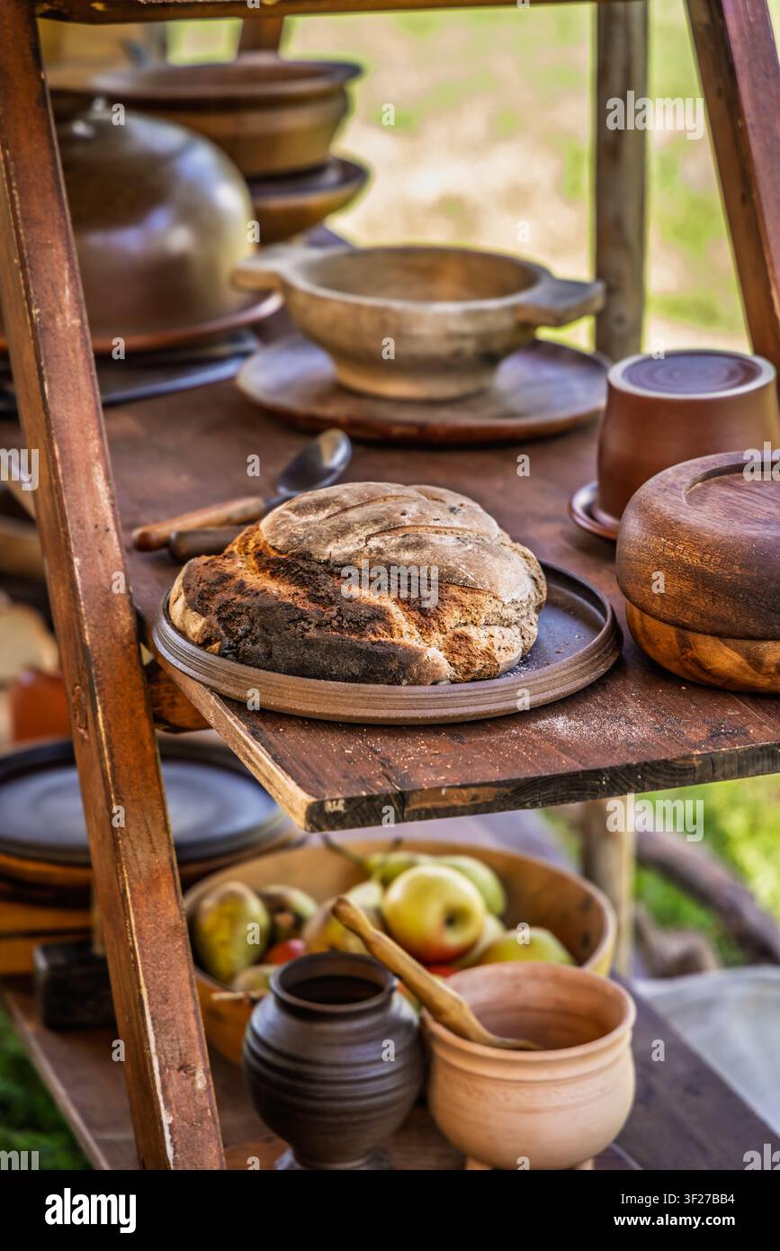 Pane rustico al lievito madre poggia su uno scaffale di legno con ceramiche antiche e frutta fresca Foto Stock